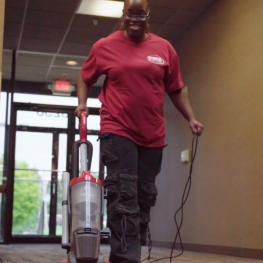 Cleaning staff member wiping the top of an office door in a corporate hallway